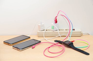 Kablolu USB adaptörleri elektrik kablosuna takılı. Işık duvarının yanındaki tahta masada şarj cihazları var.