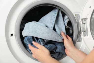 Kadın çamaşır makinesine kot pantolon koyuyor, yakın plan.