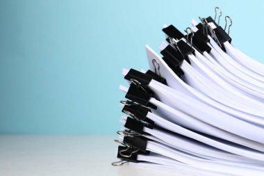 Açık mavi arkaplana karşı beyaz masanın üzerinde kağıt kağıtları olan cilt klipsleri, yakın plan. Metin için boşluk