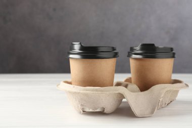 Kağıt kahve bardakları beyaz ahşap masadaki karton tutacakta, yakın plan.