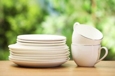 Temiz bulaşık takımları ve bardaklar ahşap masada bulanık yeşil arka plana karşı