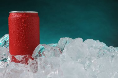 Refreshing drink in can on ice cubes against teal background, closeup