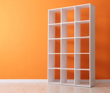 Empty shelving unit near orange wall indoors. Space for text
