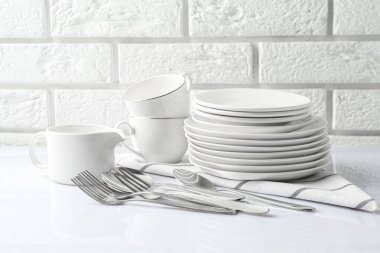 Different clean dishware on white table near brick wall