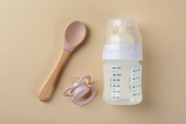 Bej arka planda süt, kaşık ve emzik ile beslenme şişesi, düz uzanma