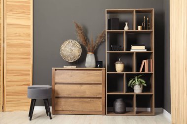 Dekorlu raf ünitesi, çekmeceler, dışkı ve katlanır ekran kapalı gri duvarın yanında