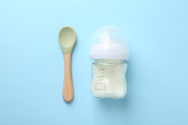 Açık mavi arka planda süt ve kaşık ile beslenme şişesi, düz yatıyordu