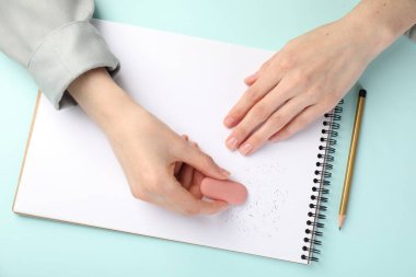 Açık mavi masada silgiye sürtünen bir kadın.