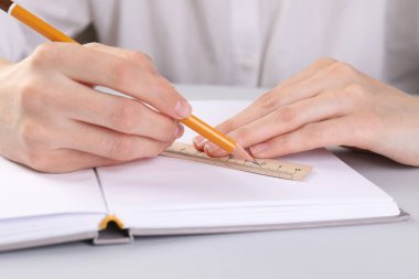 Beyaz masadaki deftere cetvel ve kalemle çizim yapan kadın, yakın plan.