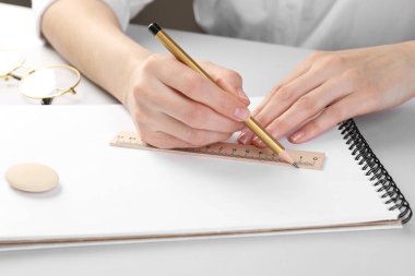 Beyaz masadaki deftere cetvel ve kalemle çizim yapan kadın, yakın plan.