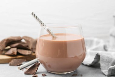 Bardakta çikolatalı süt ve açık gri masada çikolata parçaları, yakın plan.