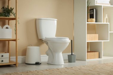 Toilet bowl, brush and necessities near beige wall in restroom