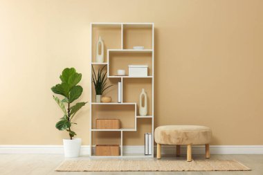 İçerideki bej duvarın yanında dekoru ve koltuğu olan raf ünitesi.