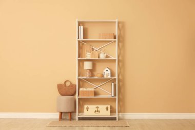 Shelving unit with decor, stool and wicker bag near beige wall indoors