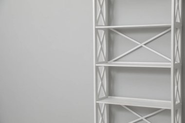 Empty shelving unit near light grey wall. Space for text