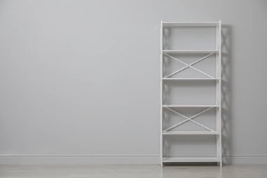 Empty shelving unit near light grey wall. Space for text