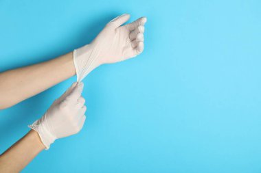 Doktor açık mavi arka plana tıbbi eldiven takıyor, yakın plan. Metin için boşluk