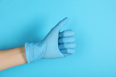 Tıbbi eldivenli doktor açık mavi arka planda baş parmak gösteriyor, yakın plan.