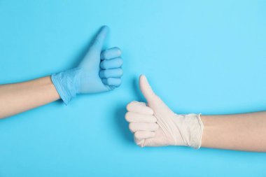 Tıbbi eldivenli doktorlar açık mavi arka planda baş parmak gösteriyor, yakın plan.