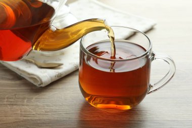 Tahta masada çaydanlıktan fincana taze demlenmiş çay dökülüyor, yakın plan.