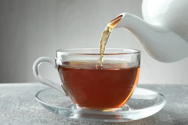 Gri masada çaydanlıktan fincana taze demlenmiş çay dökülüyor, yakın plan.