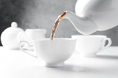 Beyaz masada çaydanlıktan fincana taze demlenmiş çay dökülüyor, yakın plan.
