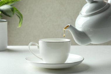 Beyaz masada çaydanlıktan fincana taze demlenmiş çay dökülüyor, yakın plan.