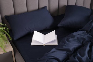Güzel koyu mavi ipek çarşaflı bir yatak ve açık bir kitap.