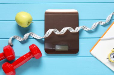 Elektronik mutfak terazisi, mezura, halterler ve elmalar açık mavi ahşap masada, düz yerde. Diyet