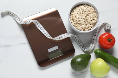 Elektronik mutfak ölçeği, mezura ve beyaz mermer masa üzerindeki ürünler düz konum. Diyet