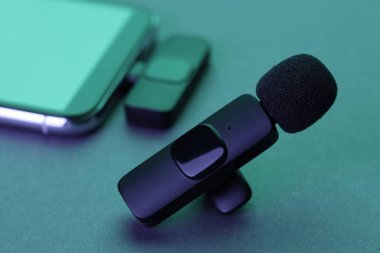 Lavalier mikrofon ve kablosuz alıcısı olan akıllı telefon karanlık masada neon ışıklarda, yakın plan.