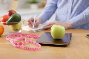 Mutfak terazisinde elmayı tartan kadın, kapalı masa, yakın plan.