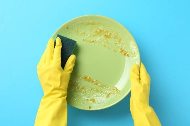 Açık mavi arka planda süngerle kirli tabakları yıkayan adam, üst görünüm