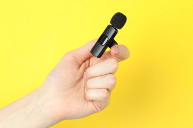 Sarı arka planda lavalier mikrofon tutan kadın, yakın plan.