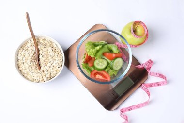 Elektronik mutfak terazileri salata, elma, yulaf ve ölçüm bantları beyaz, üst görünümde izole edilmiş.