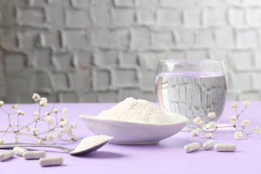 Kasede kolajen tozu, kaşık, haplar, bir bardak su ve kapalı menekşe masasında çingene çiçeği.