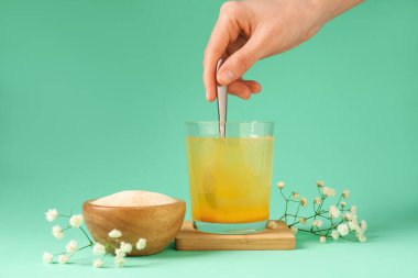 Turkuaz arka planda suda kolajen tozu karıştıran kadın, yakın plan.