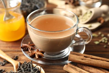 Aromatik Masala çayı fincanda, baharatlar, kuru yapraklar ve bal ahşap masada, yakın plan.