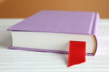 Kahverengi arkaplana karşı beyaz ahşap masa üzerinde kırmızı kurdele yer imi olan kitap, yakın plan