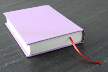 Koyu desenli masa üzerinde kırmızı kurdele yer imi olan kitap, yakın plan.