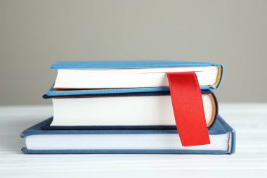 Kırmızı kurdele yer imi ve beyaz ahşap masa üzerinde renkli kitap gri arkaplan, yakın plan