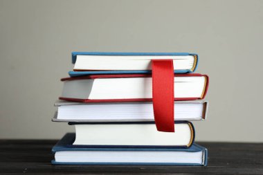 Kırmızı kurdele yer imi ve ahşap masadaki renkli kitap gri arkaplanda, yakın plan