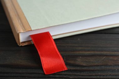 Ahşap masada kırmızı kurdele yer imi olan bir kitap, yakın plan.