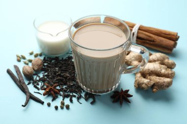 Cam fincanda Aromatik Masala çayı, baharatlar, kuru yapraklar ve açık mavi arka planda süt, yakın plan
