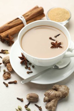 Aromatik Masala çayı bardakta, baharatlar ve kahverengi şeker açık gri masada, yakın plan.