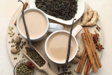 Açık gri masada fincanlarda, baharatlarda ve kuru yapraklarda Aromatik Masala çayı.