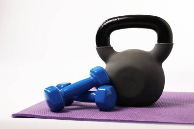 Kettlebell ve dambıllar beyaz arkaplana karşı fitness minderinde