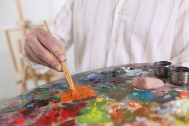 Sanatçının stüdyosunda boyaları palette karıştıran adam, yakın plan.