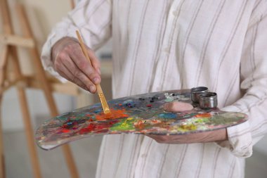 Sanatçının stüdyosunda boyaları palette karıştıran adam, yakın plan.