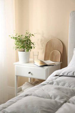 Yatağın yanında kitap, dekor ve bir bardak su olan komodin.